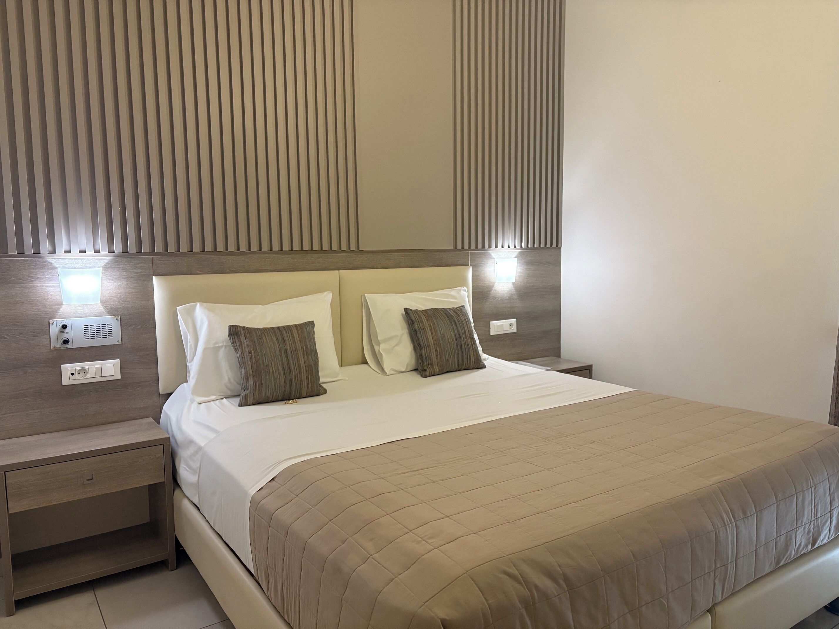 A hotel room with a bed, bedside tables, and a wall-mounted light fixture.