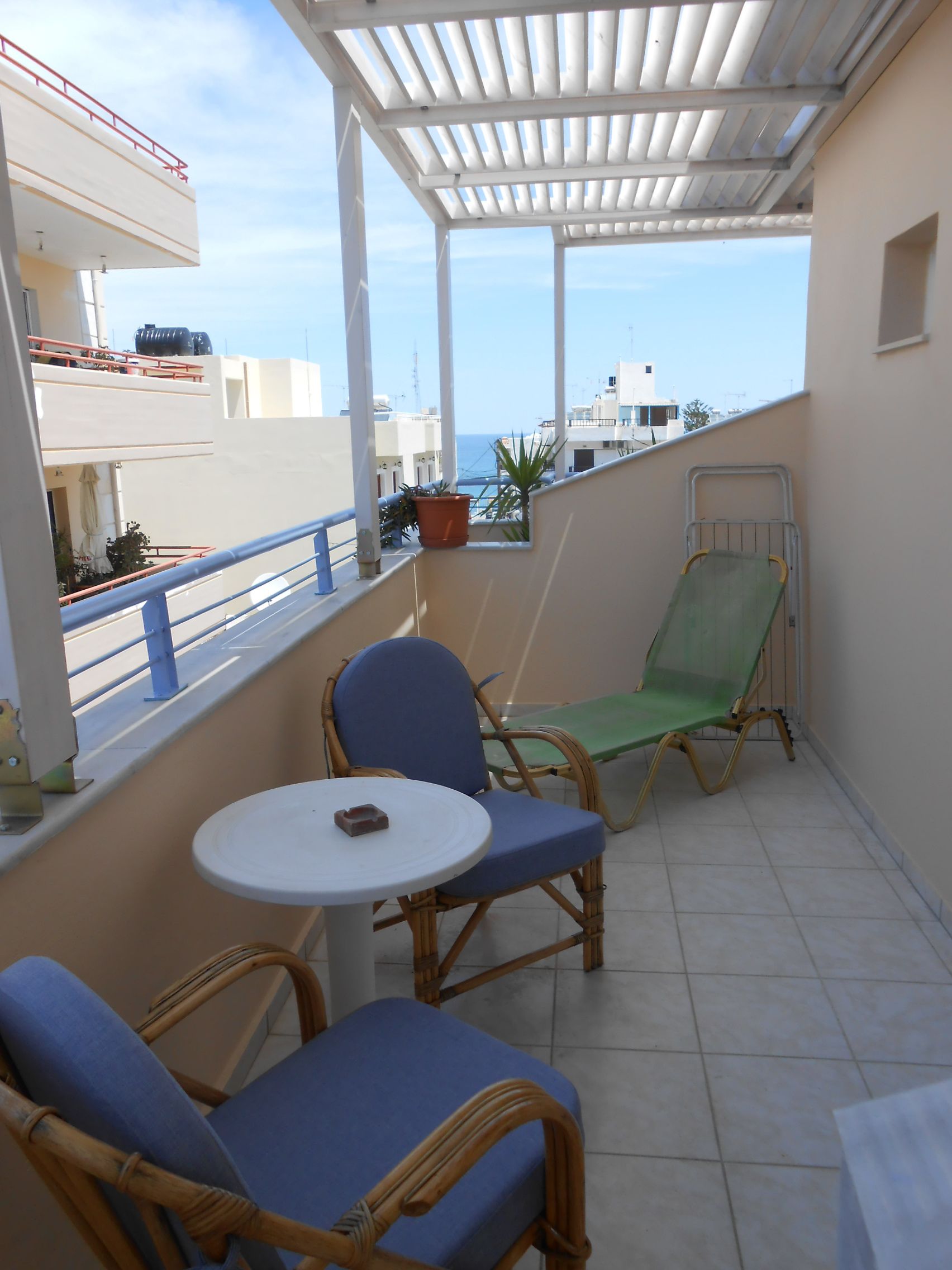 A balcony with two wicker chairs and a small table, overlooking a cityscape.
