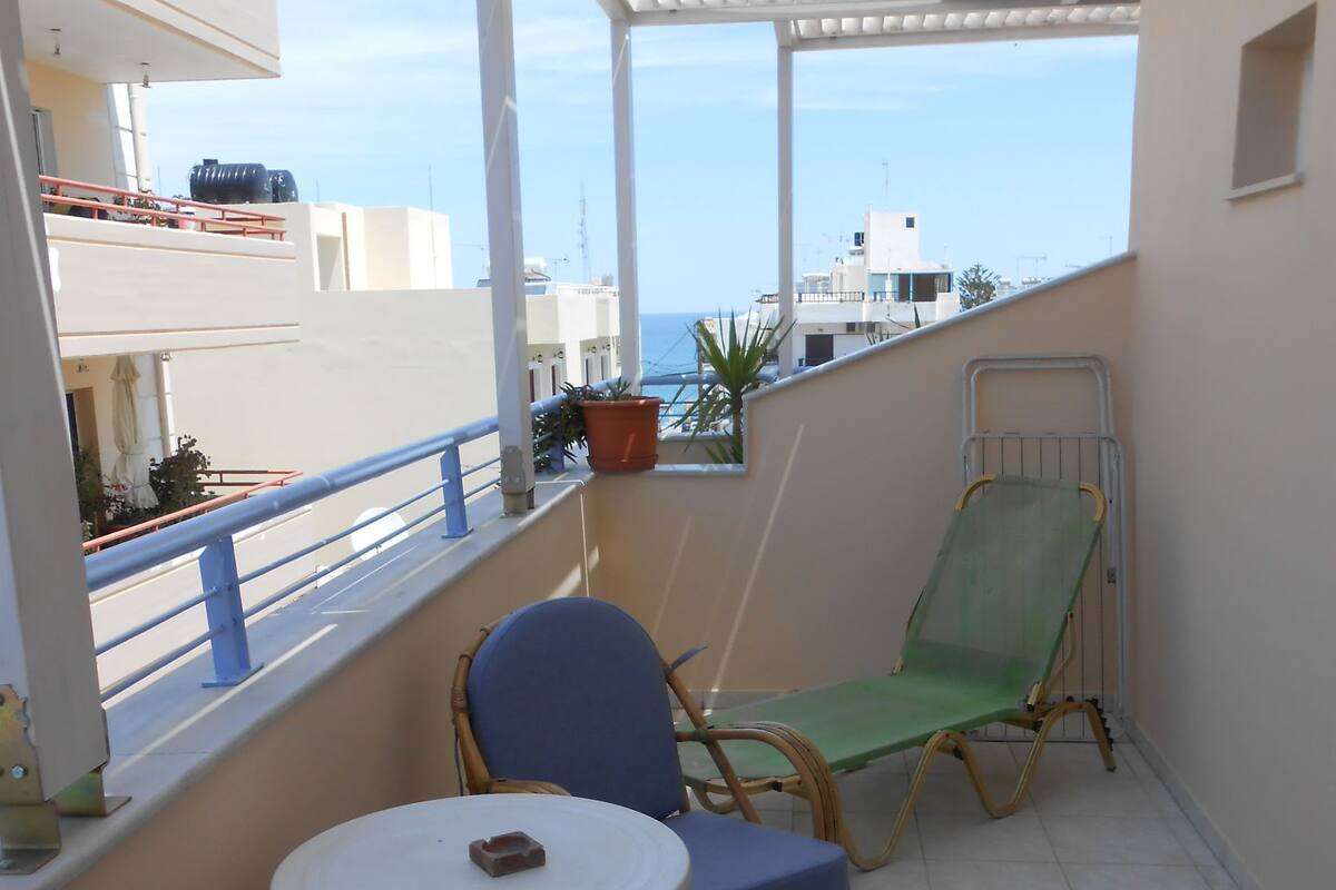 A balcony with two wicker chairs and a small table, overlooking a cityscape.