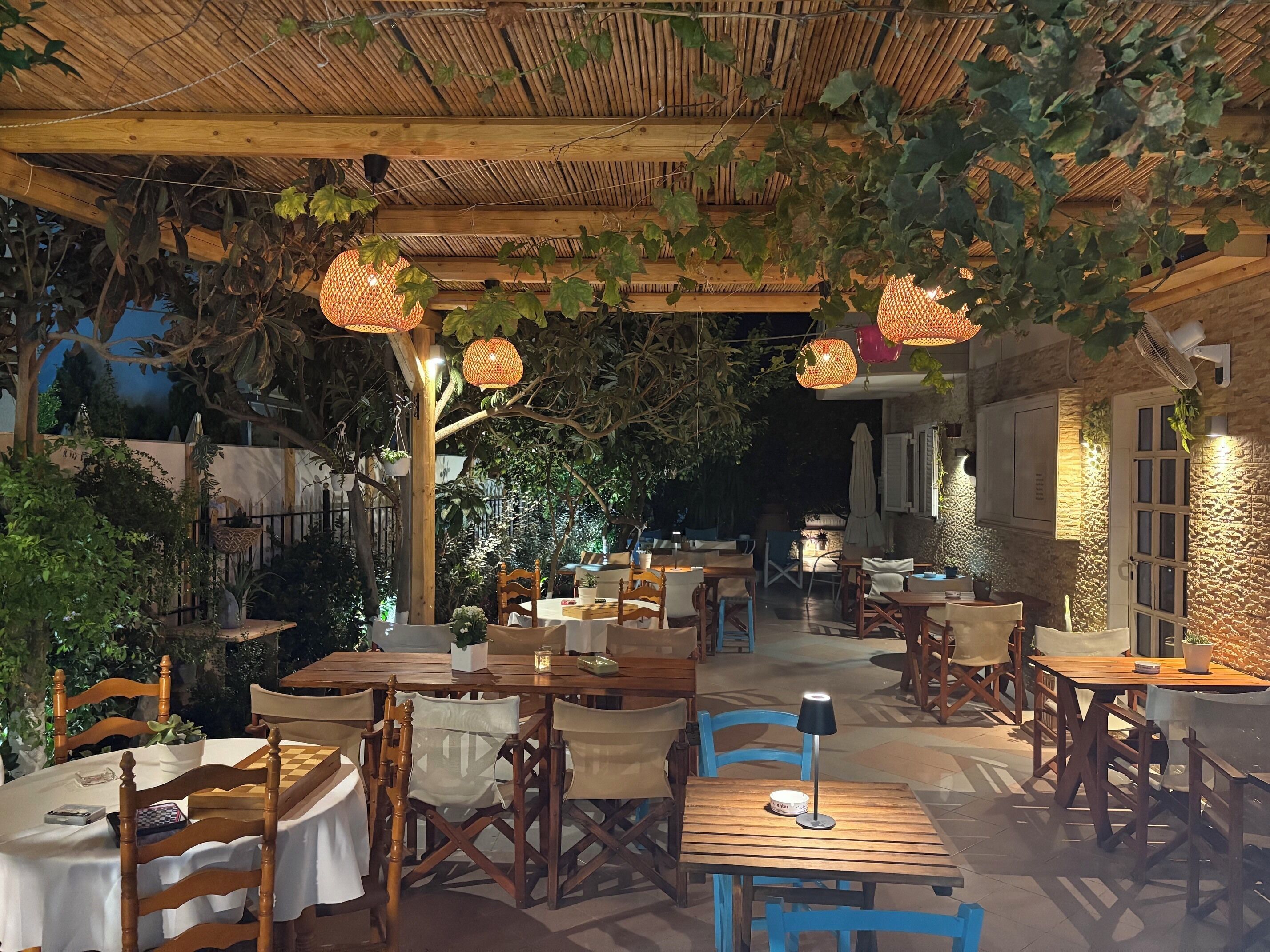 Un espacio para comer al aire libre con mesas y sillas de madera, faroles colgantes y techo de bambú.