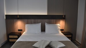 A modern hotel room with a large bed, two bedside tables, and a headboard with built-in lighting. - Voula Hotel (Hersonissos)