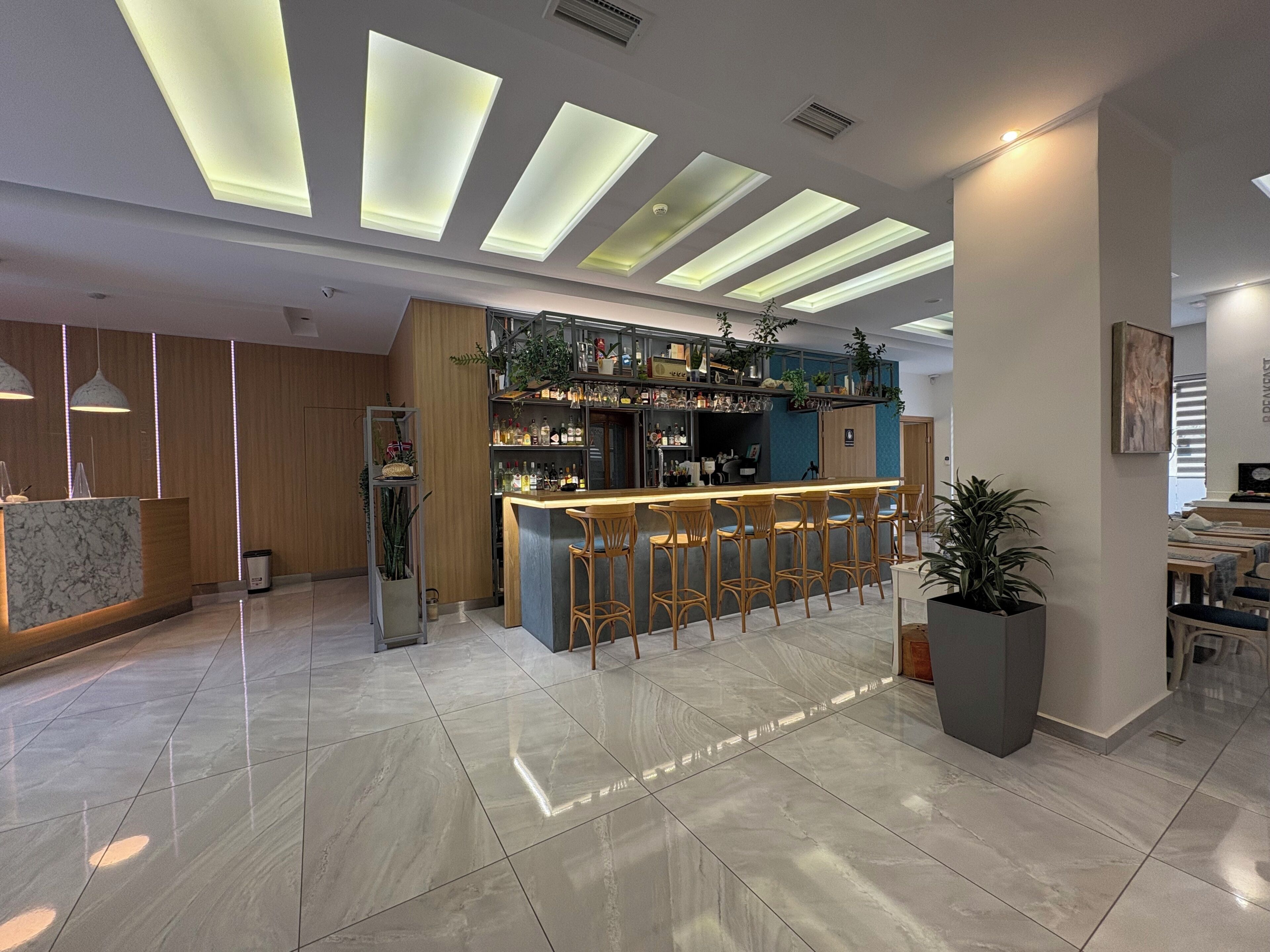 A modern bar area with a marble countertop, bar stools, and a variety of bottles and glasses.