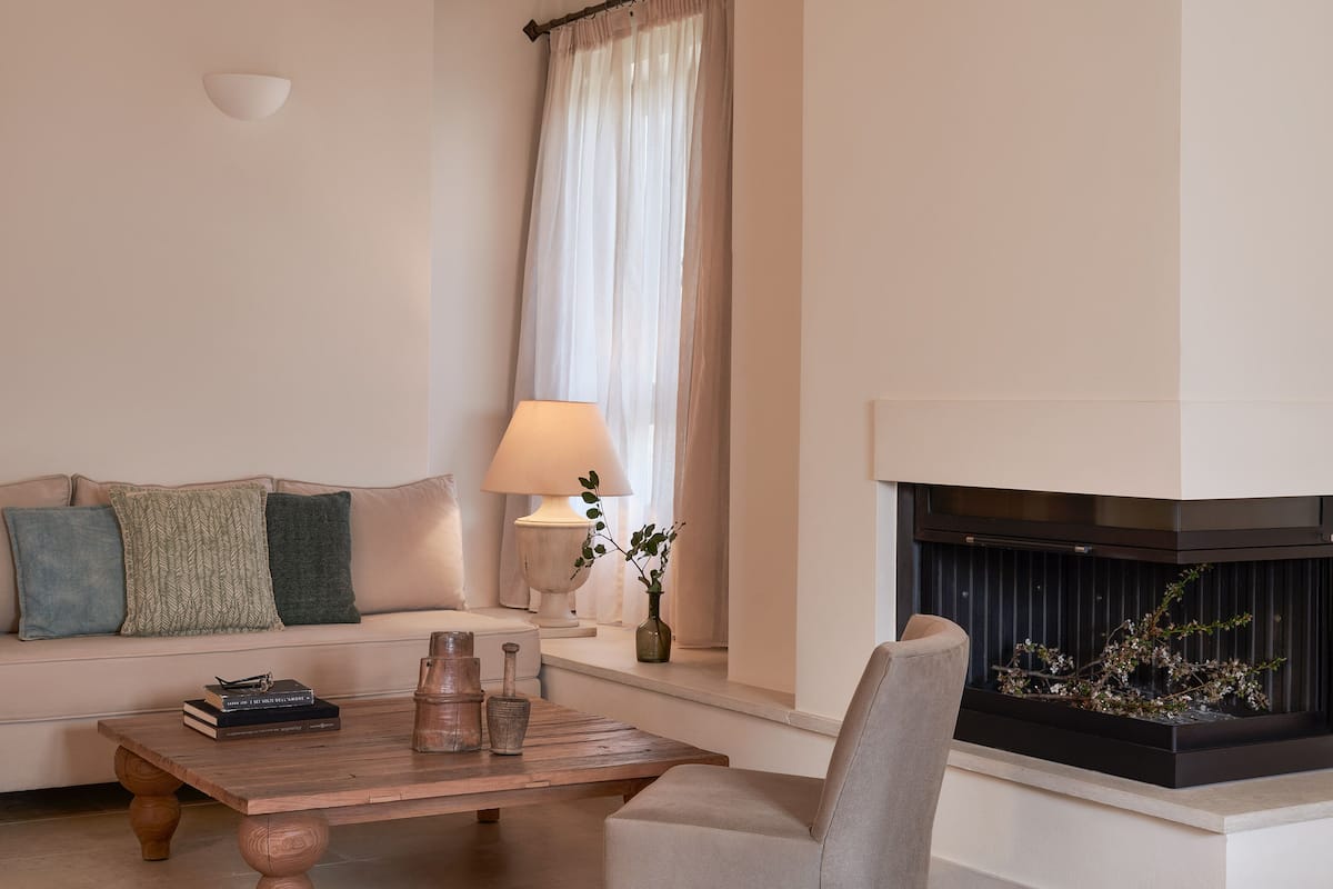 A living room with a sofa, a coffee table, a lamp, a vase with branches, and a fireplace.