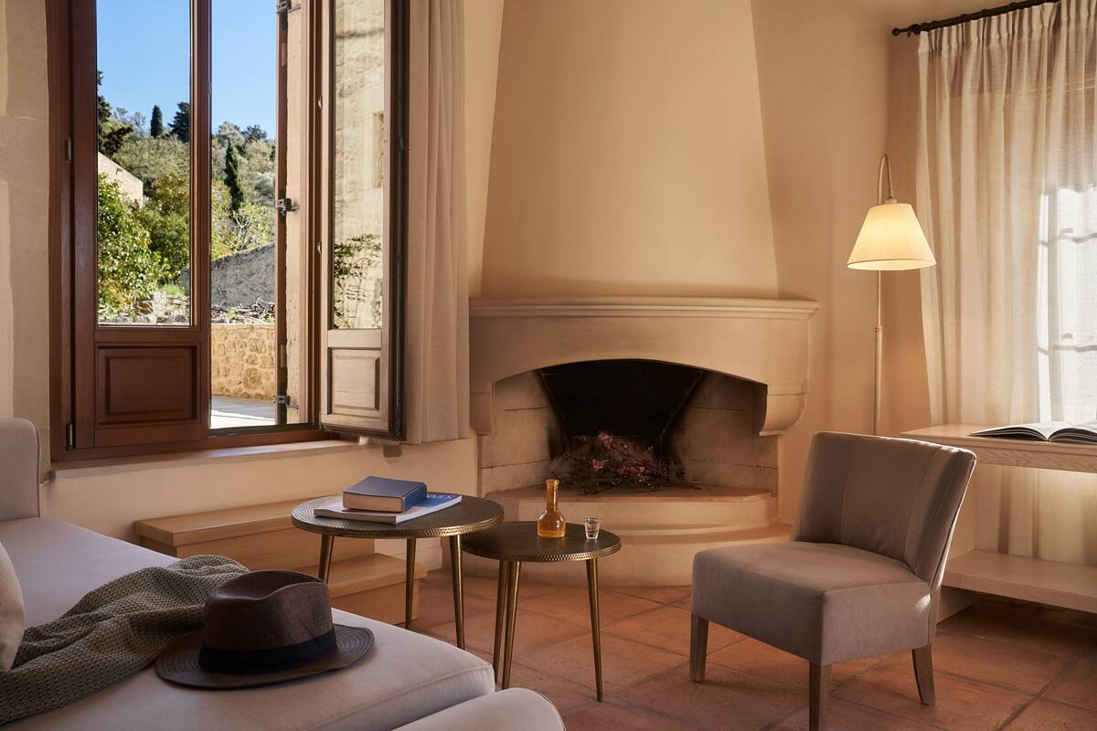 A cozy room with a fireplace, a sofa, a chair, and a small table with a book and a bottle.