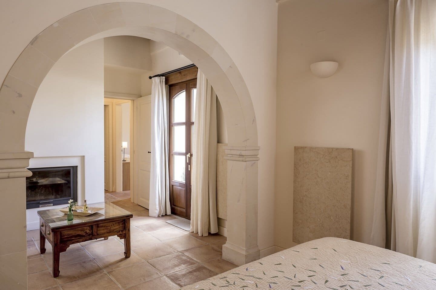 A room with an arched doorway, a fireplace, a bed, and a small table with a tray.