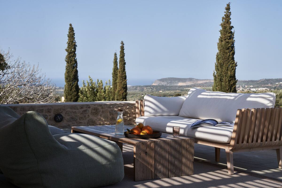 A terrace with a white sofa, a wooden coffee table with fruits and a glass, and a green bean bag.