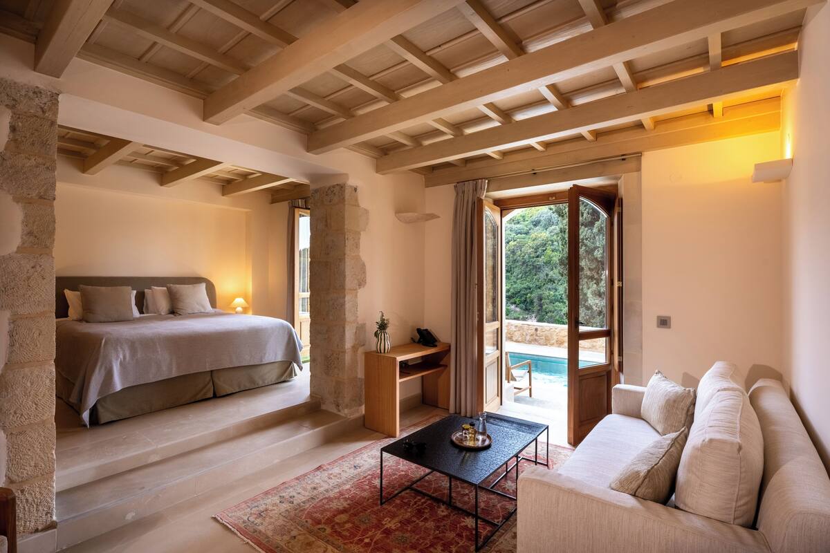 A bedroom with a bed, a desk, a sofa, and a view of the outdoors.