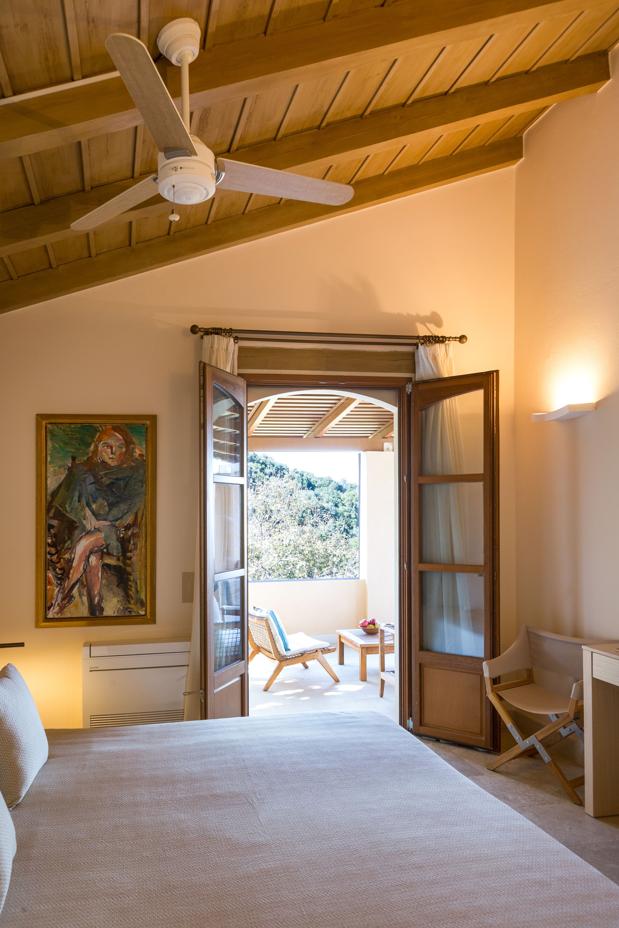 Un dormitorio con cama, ventilador de techo, un cuadro y vistas al exterior.