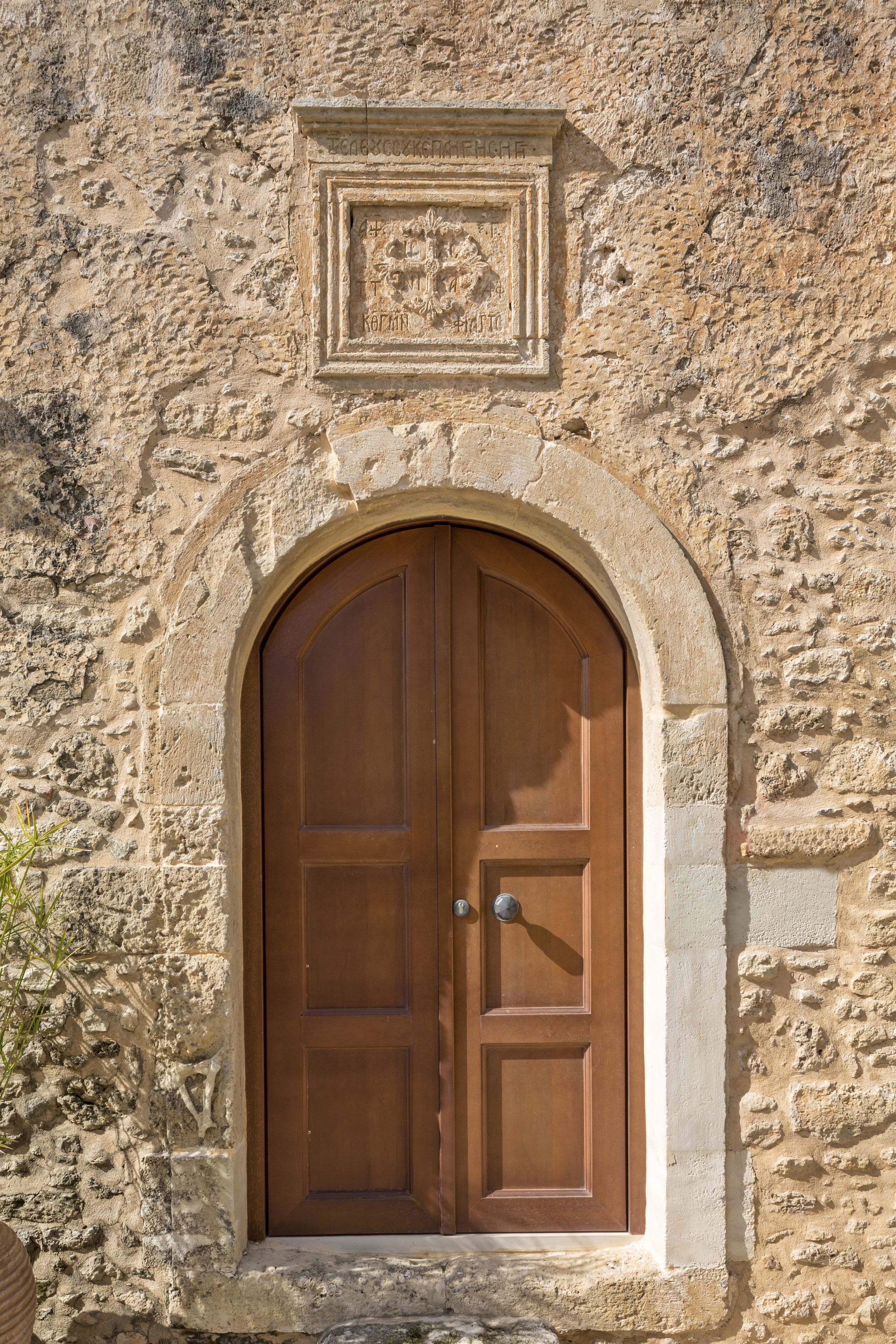 A stone building with a wooden double door framed by an arch.