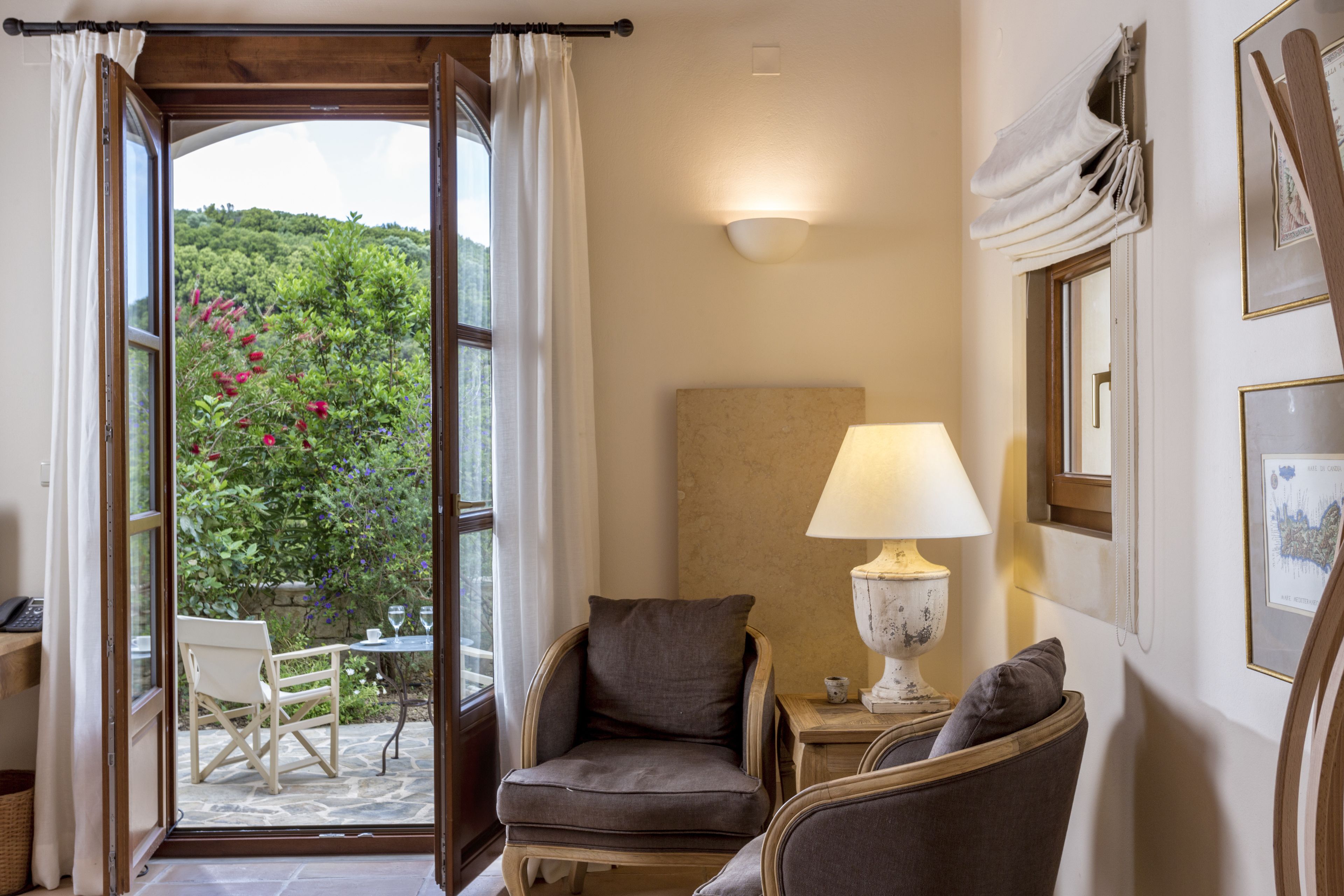 Quarto com vista para um jardim, uma cadeira, uma mesa, um abajur e um quadro pendurado na parede.