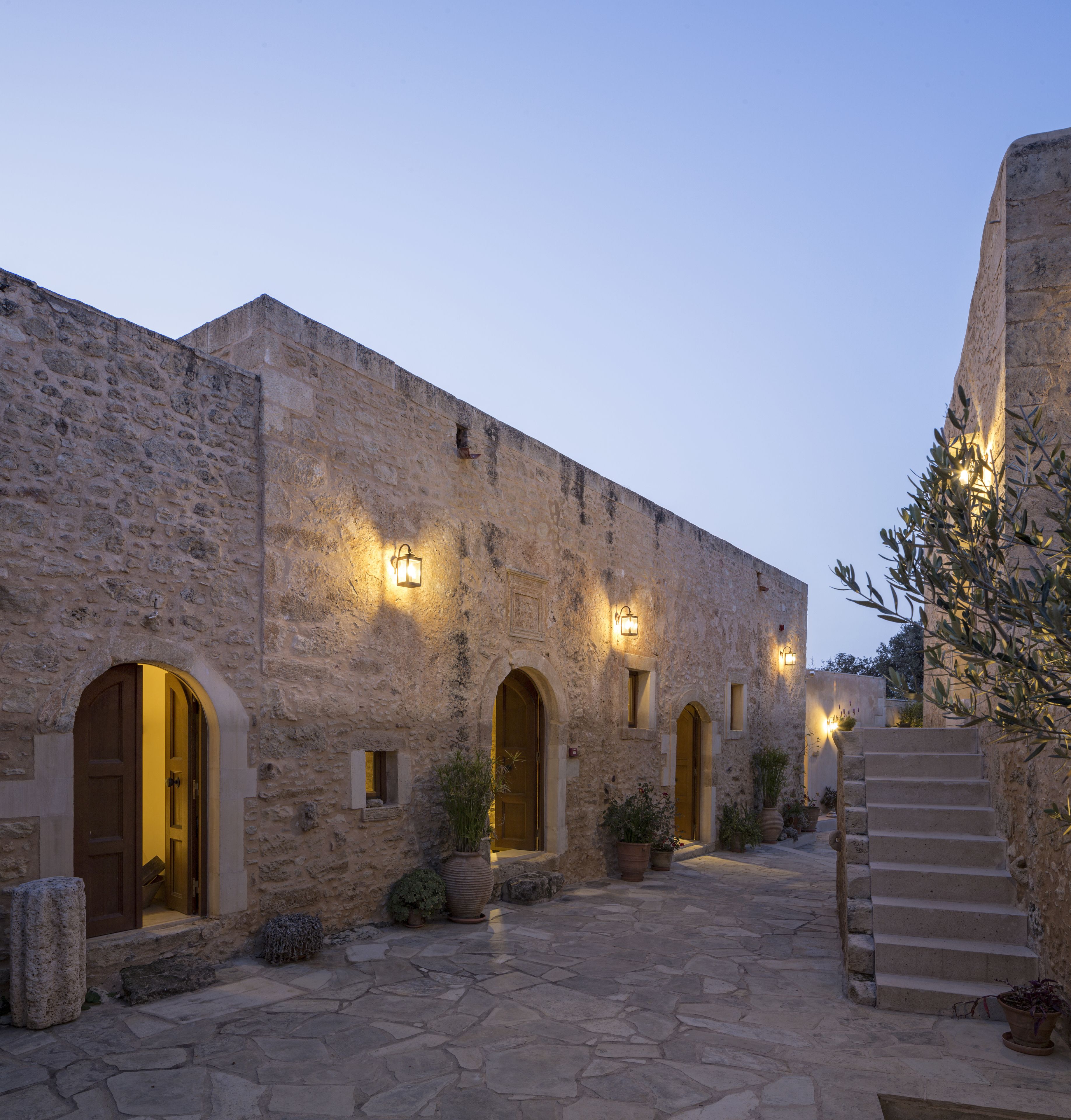 A stone building with arched doorways and windows, illuminated by wall-mounted lights.
