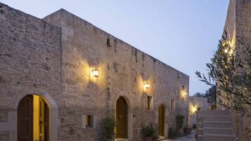 A stone building with arched doorways and windows, illuminated by wall-mounted lights.