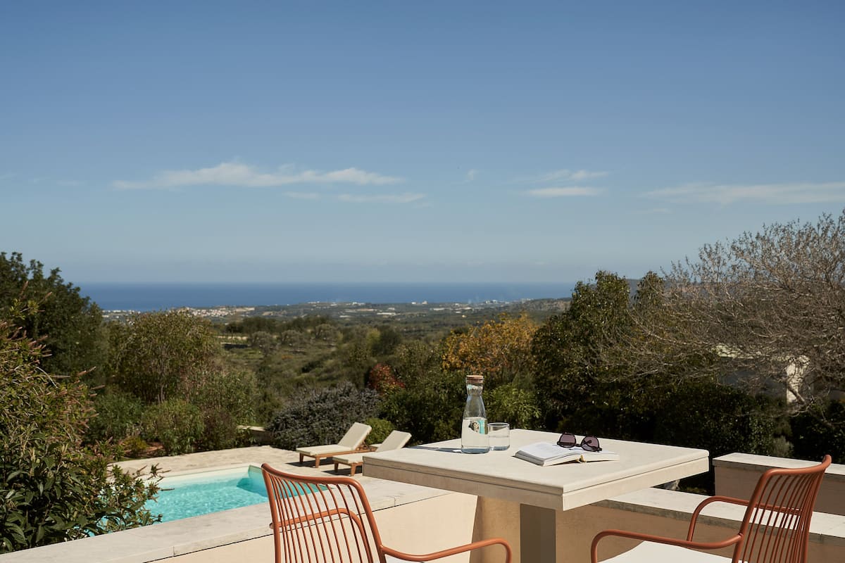 A terrace with a pool, two chairs, a table, and a bottle of water.