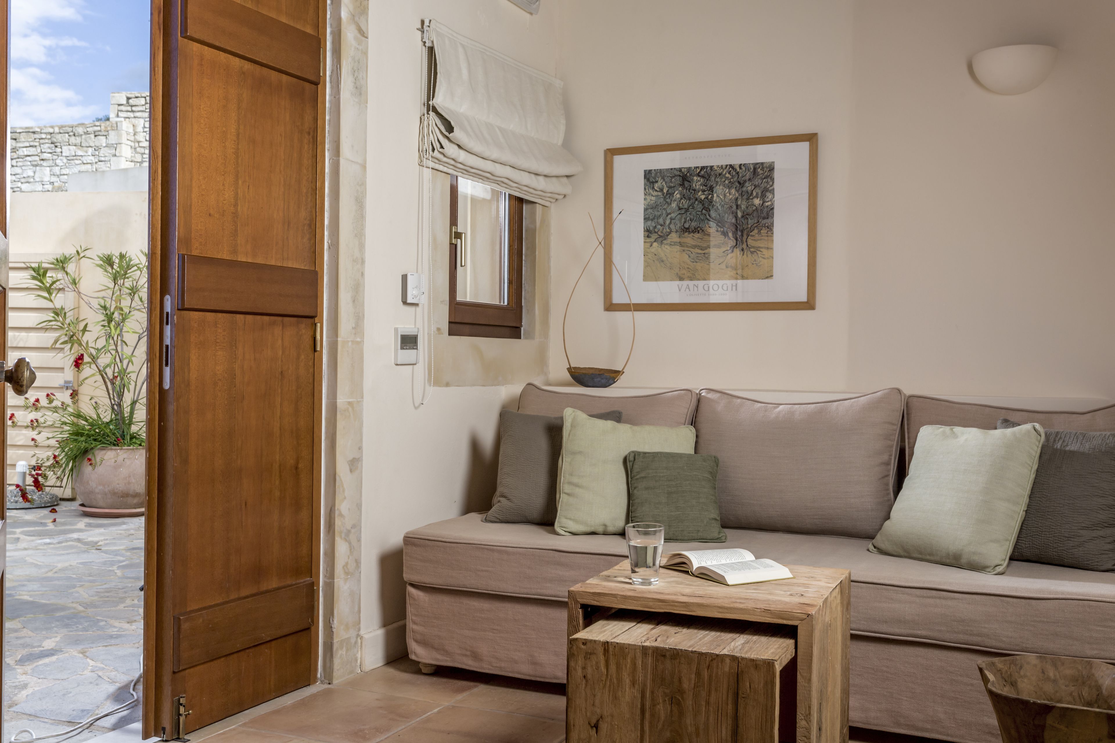 Ein Wohnzimmer mit einem beigefarbenen Sofa, einem Holztisch, einem Fenster mit weißem Rollo, einem gerahmten Bild an der Wand und einem Blumentopf.