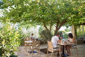 An outdoor dining area with stone tables and wicker chairs, surrounded by greenery and trees. - Kapsaliana Village Hotel (Rethymno)