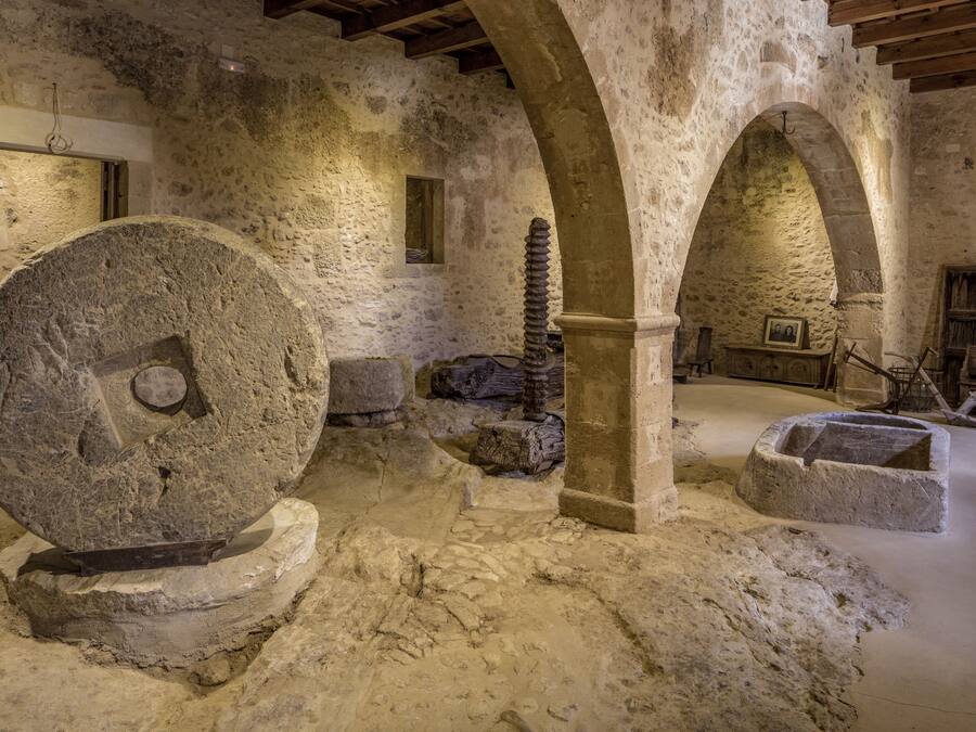 A stone interior with a large grinding wheel, stone benches, and an arched ceiling.