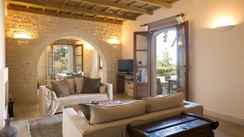 Una sala de estar acogedora con un arco de piedra, un sofá, un banco de madera y un televisor.