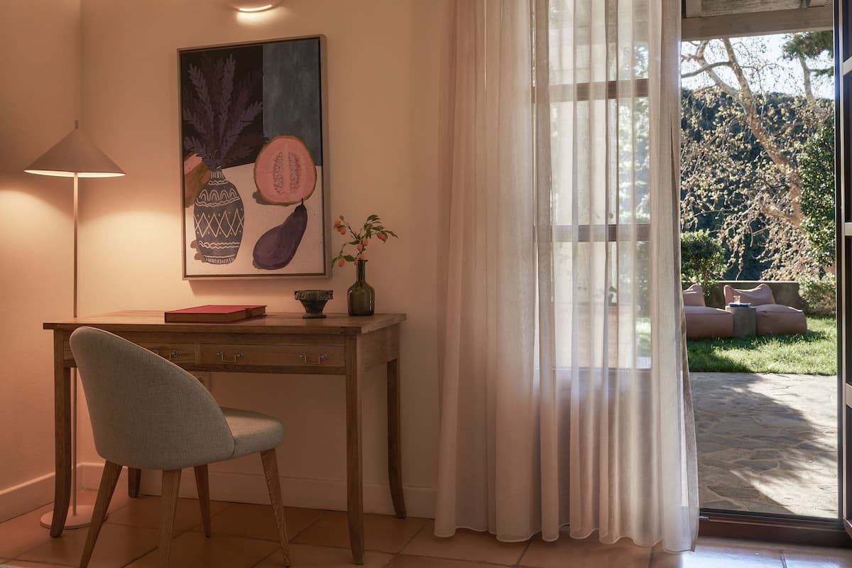 A room with a desk, chair, and a large window with sheer curtains.