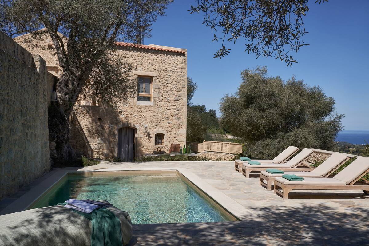 A stone building with a pool and lounge chairs.