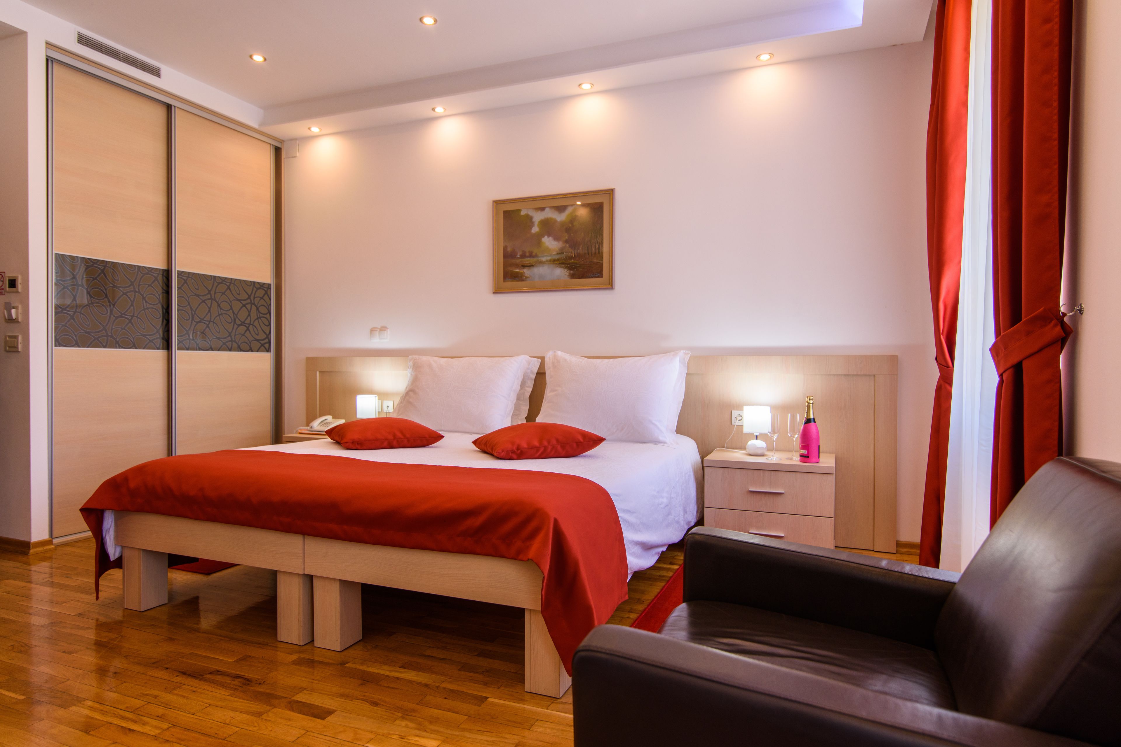 Un dormitorio ordenado con cama, mesitas de noche, una silla y un cuadro en la pared.