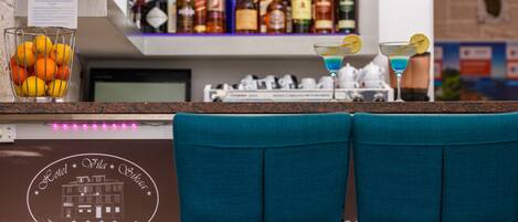 A bar area with a counter, a glass container of oranges, and two blue chairs.