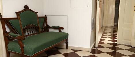 Una habitación con piso a cuadros, un banco de madera con cojín verde y una puerta blanca al fondo.