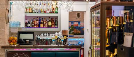 Una zona de bar con mostrador, taburetes y estantes llenos de botellas.