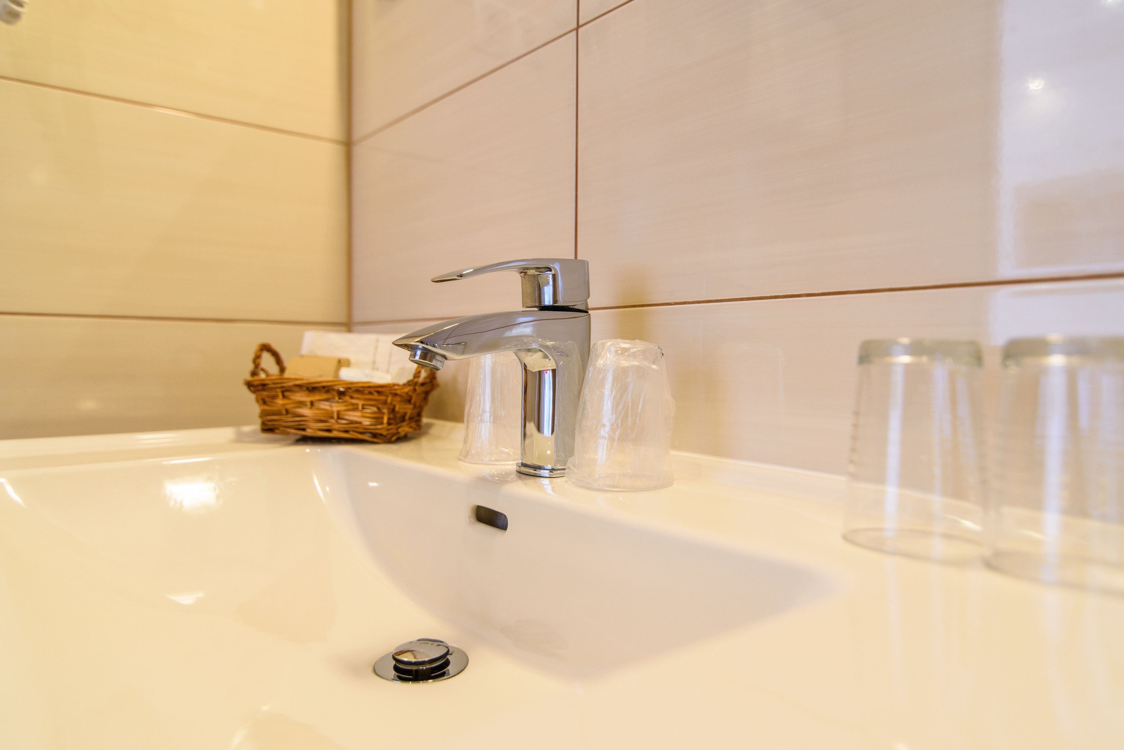A bathroom sink with a chrome faucet, a wicker basket, and clear glass bottles.