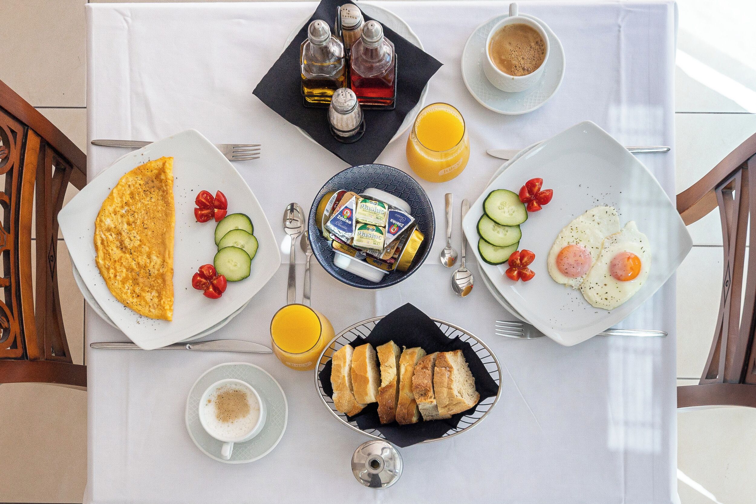 Une table de petit-déjeuner avec des assiettes contenant des œufs, des toasts et du jus, ainsi que des condiments et des couverts.