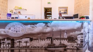 A hotel reception area with a view of a historic town, a reception desk, and a display of local products. - Hotel Sikaa (Trogir)