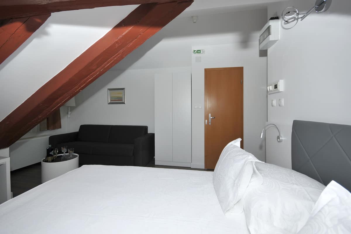 A hotel room with a bed, a black sofa, a white wardrobe, and a wooden door.