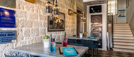 A restaurant with stone walls, wooden beams, and a checkered floor. There are tables with chairs, a menu, and a sign for room rental.