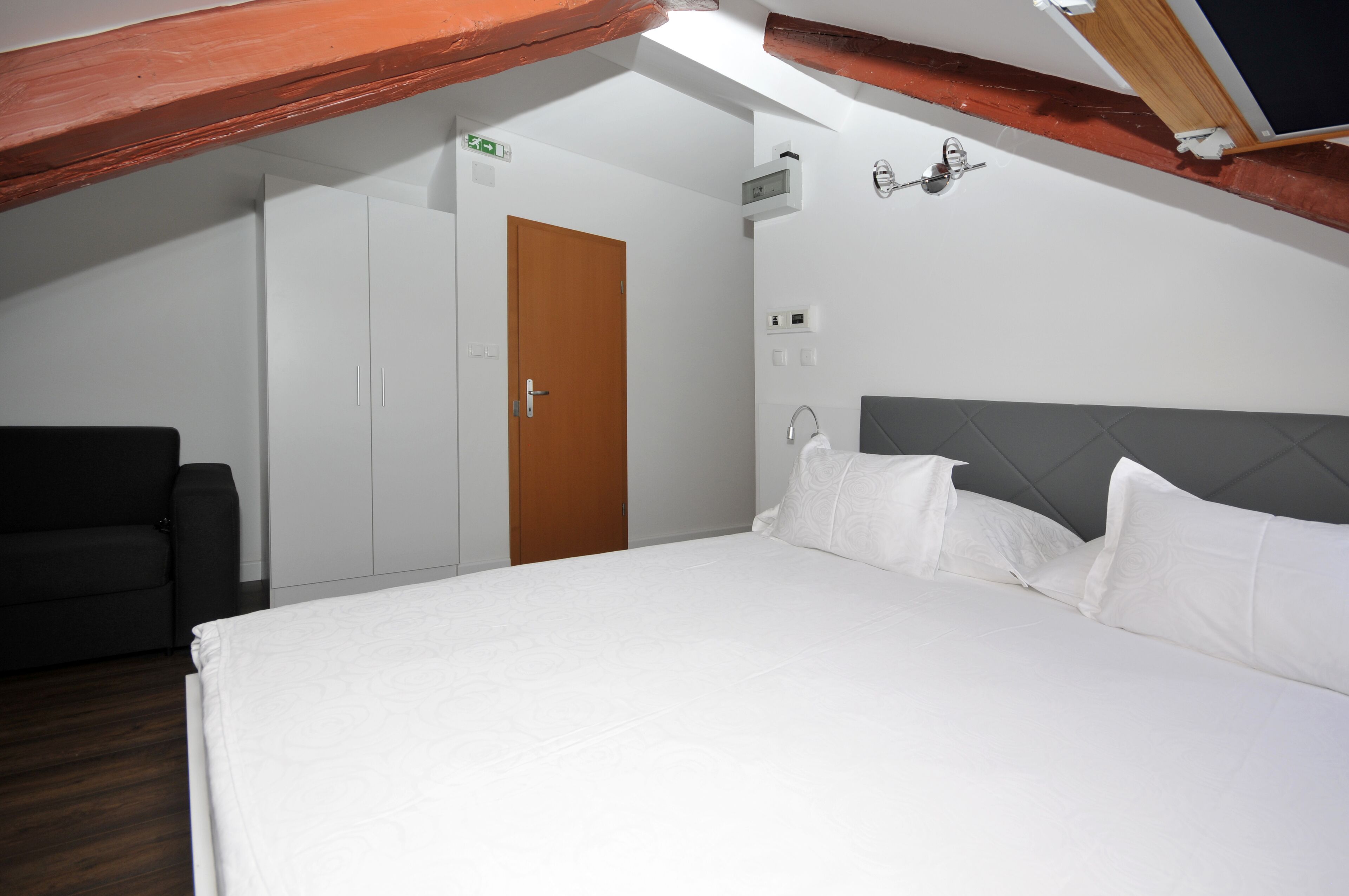 A bedroom with a bed, a wardrobe, a door, and a ceiling with exposed beams.