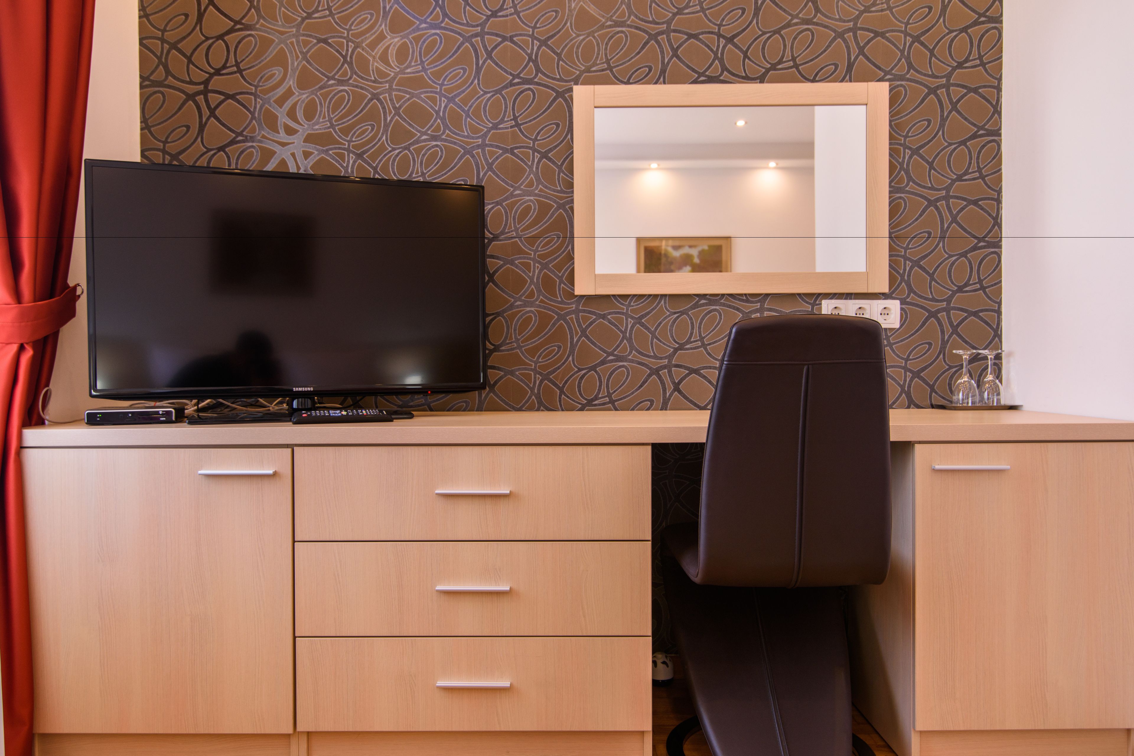 Ein modernes Hotelzimmer mit Flachbildfernseher, Spiegel und Schreibtisch mit Schubladen.