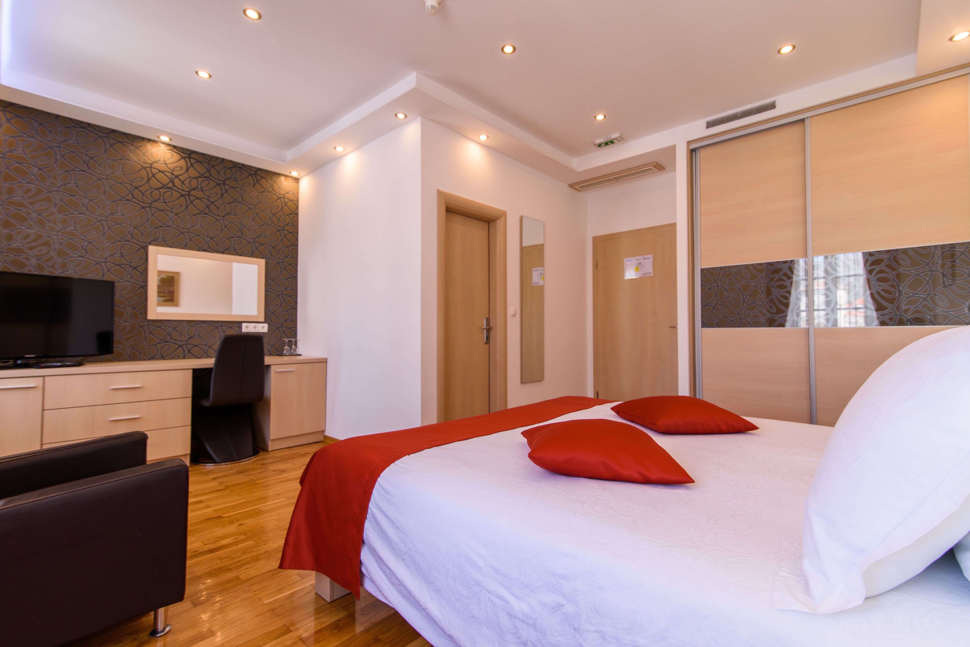 Una habitación de hotel moderna con una cama grande, un escritorio con silla, televisión y armario.