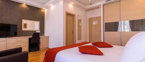 Una habitación de hotel moderna con una cama grande, un escritorio con silla, televisión y armario.