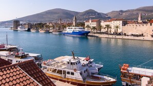 A harbor with boats docked, a historic stone wall, and a hill in the background. - Hotel Sikaa (Trogir)