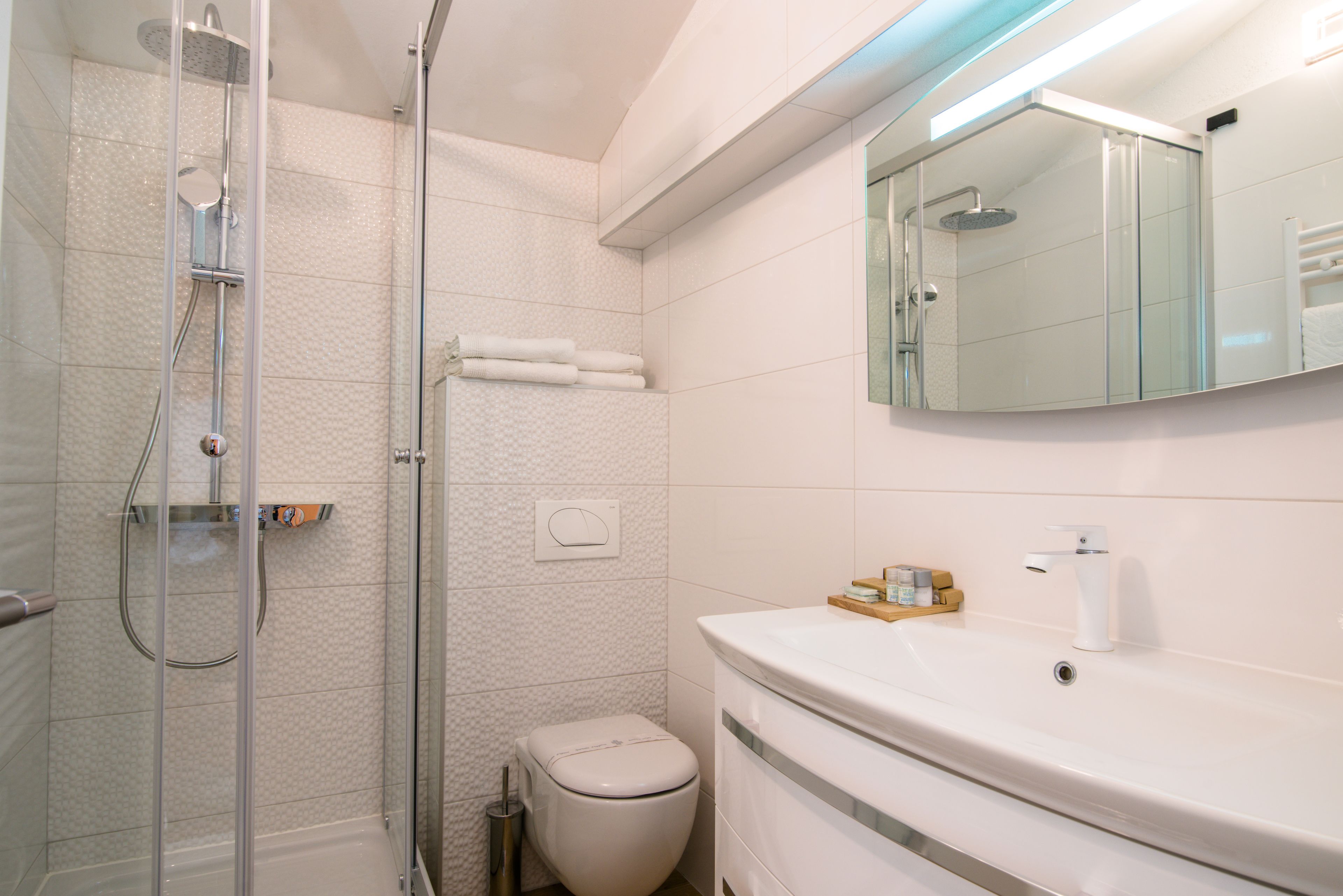 Un bany modern amb dutxa tancada amb vidre, un vàter i un lavabo amb mirall a la part superior.