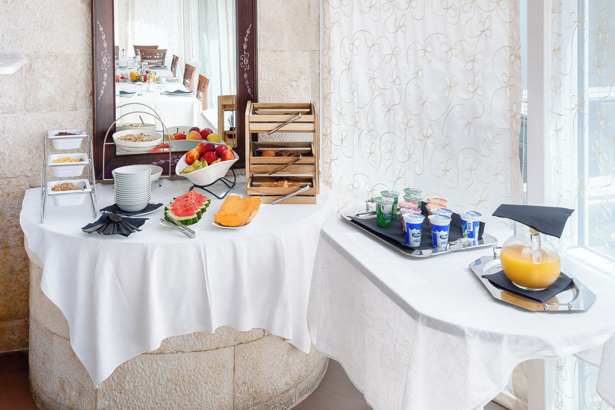 A breakfast buffet setup with various food items and beverages, a fruit bowl, and a juice dispenser.