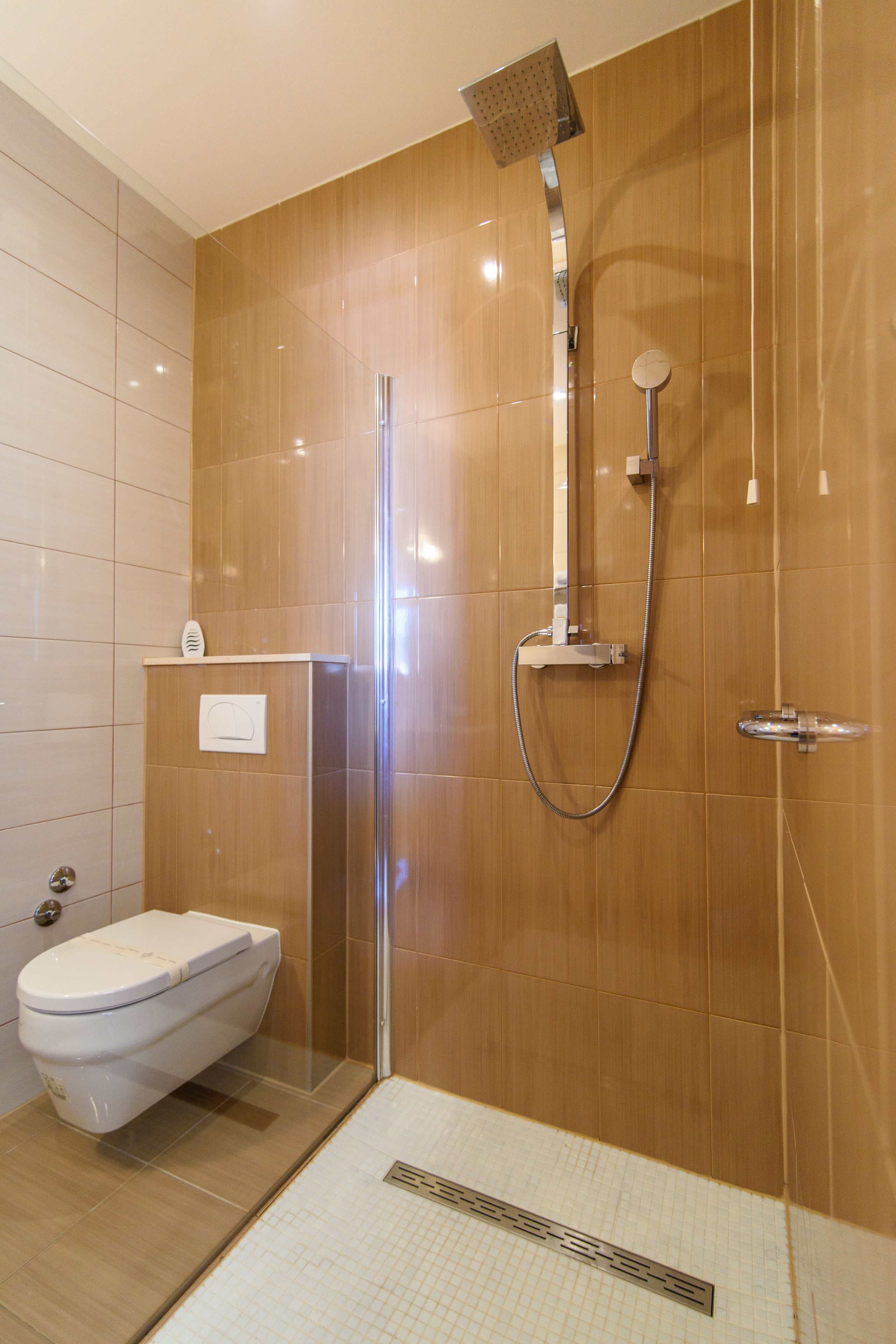 Un bany modern amb plat de ducha tancat per vidre, un vàter i un lavabo amb mirall.
