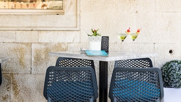 Un café con un cartel que dice "Vila Sikaa Travel agency Caffe Bar" y dos sillas frente a una mesa con una planta y dos bebidas.