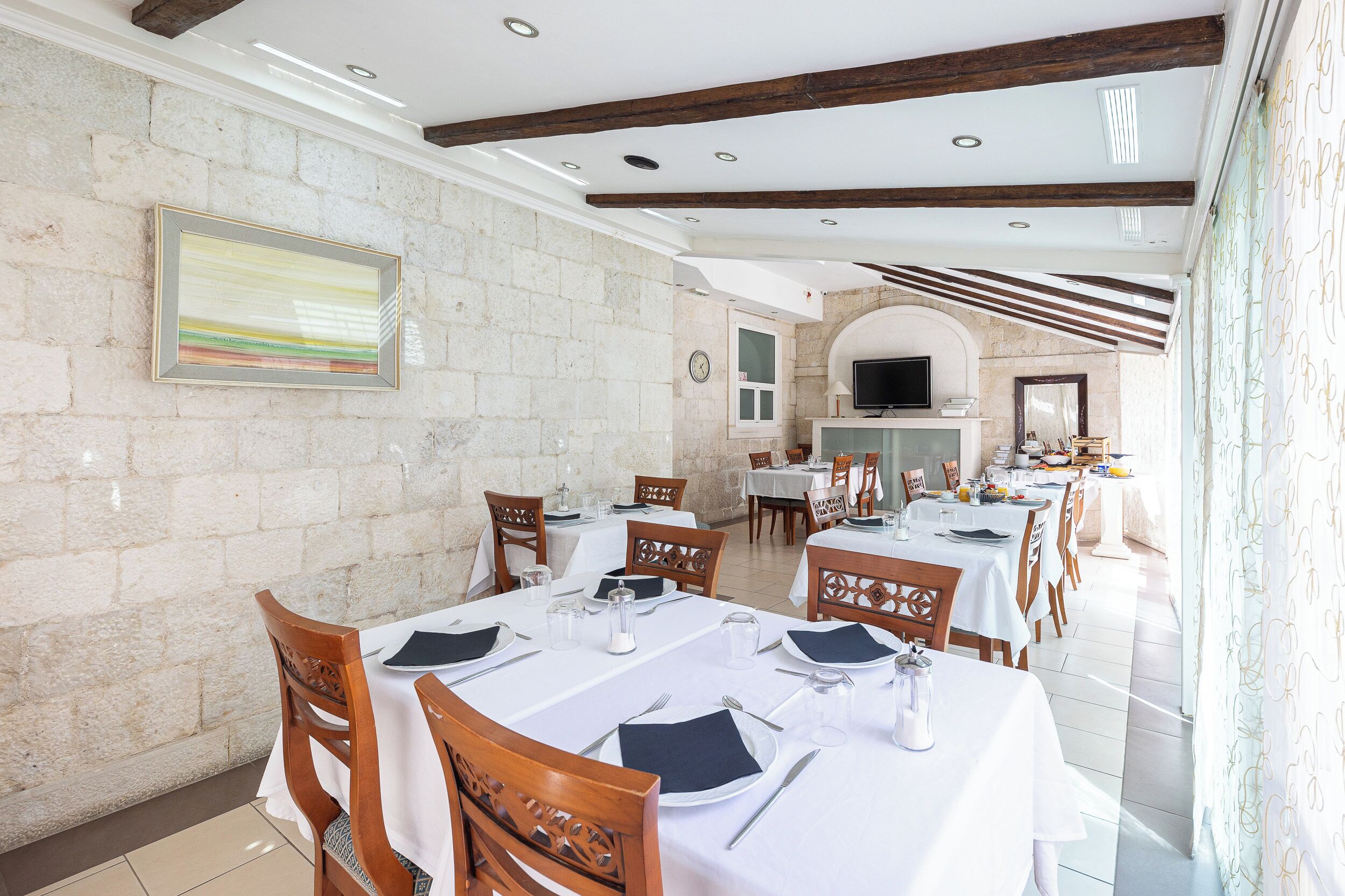 Un comedor con mesas dispuestas para el servicio, paredes de piedra y un televisor montado en la pared.