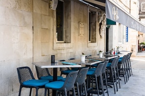 An outdoor seating area with tables and chairs, a stone wall, and a sign for a hotel. - Hotel Sikaa (Trogir)
