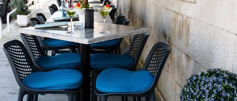 Una mesa con sillas acolchadas azules, una bebida con adornos y una pequeña planta en maceta.