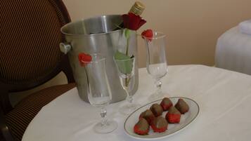 Una mesa con un balde metálico, una rosa, dos copas de vino y un plato de fresas cubiertas de chocolate.