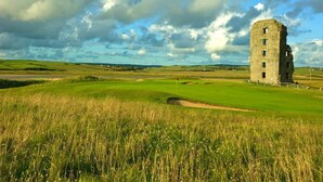 A historic stone tower in a grassy field with a golf course in the background. - Shamrock Inn Hotel (Lahinch)