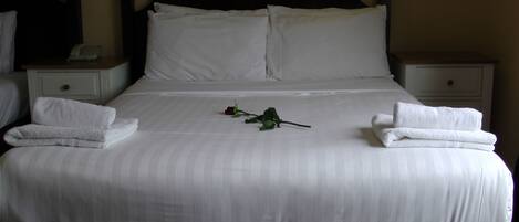 A neatly made bed with white linens and two folded towels on each side.