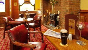 A cozy pub interior with leather chairs, a round table, a fireplace, and a Guinness beer on the table. - Shamrock Inn Hotel (Lahinch)