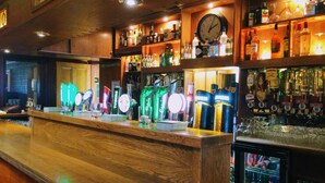 A bar area with multiple beer taps, a clock, and shelves stocked with various bottles. - Shamrock Inn Hotel (Lahinch)