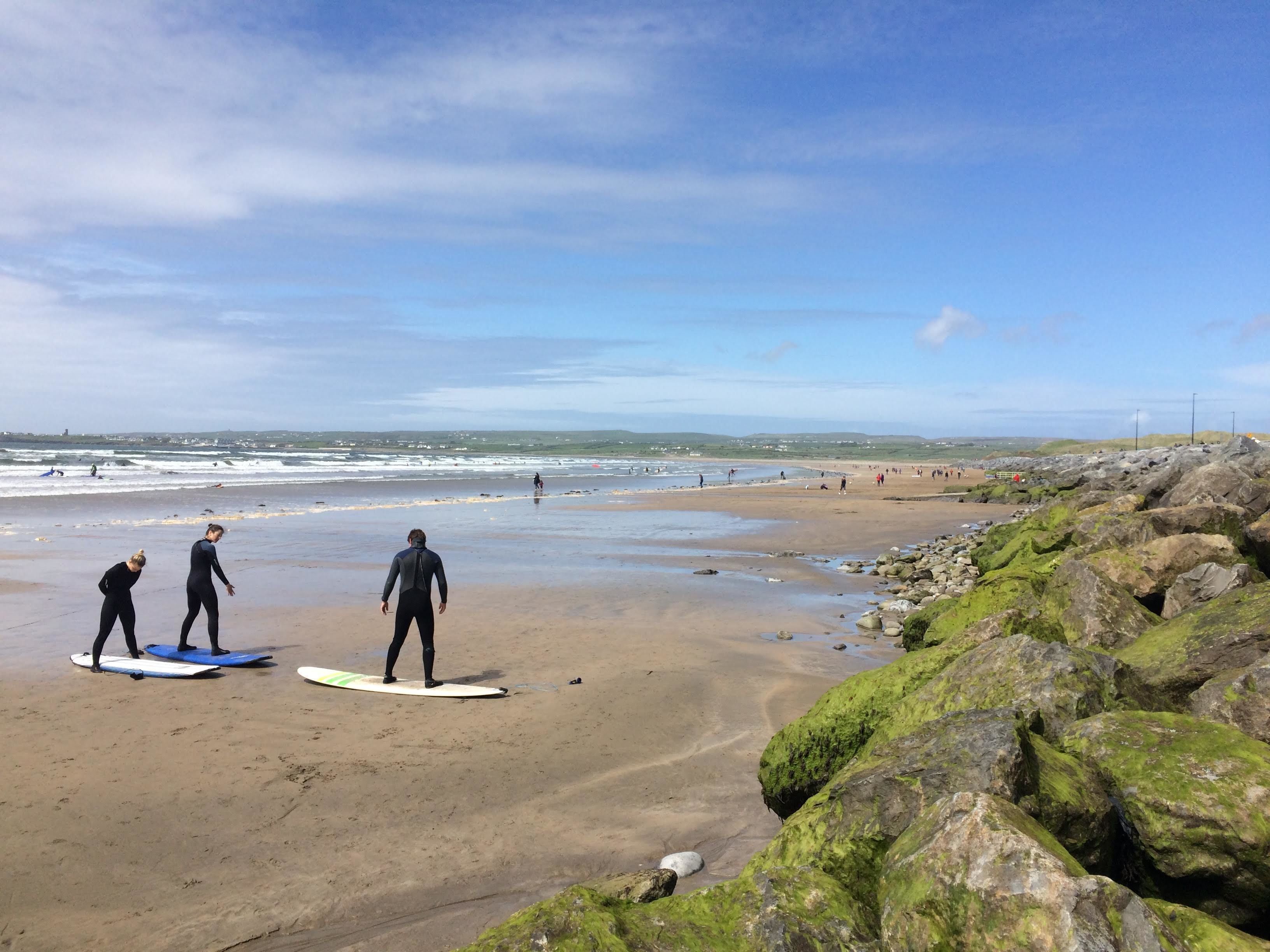 A beach with people on surfboards, rocky shoreline, and distant waves.